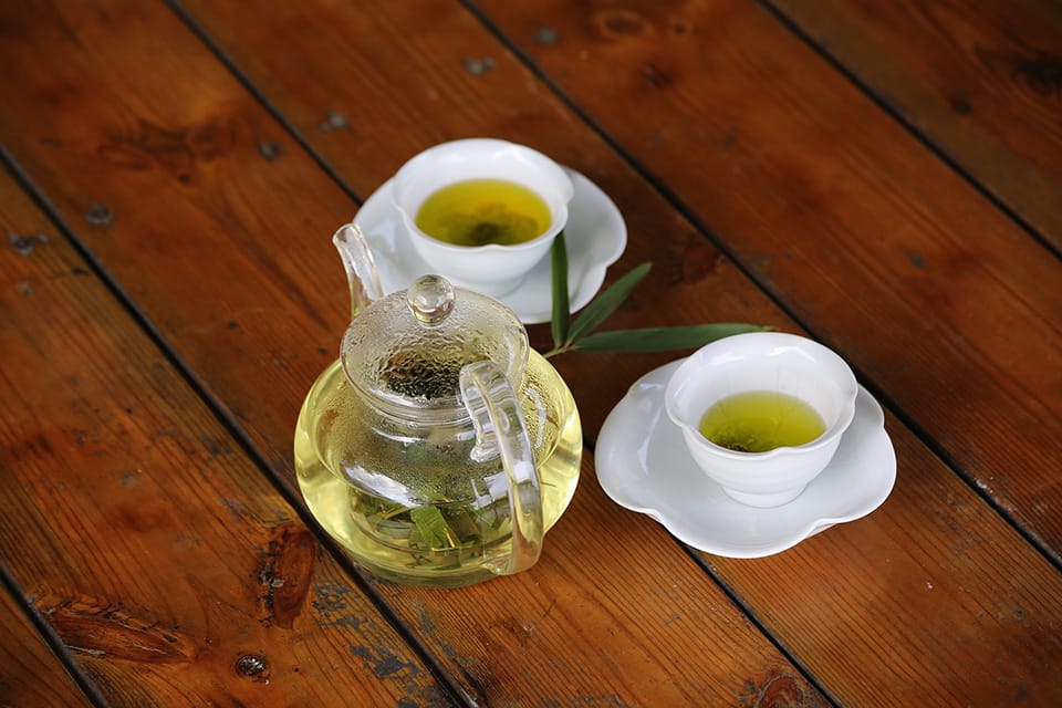 Two cups of bamboo tea and a glass can with bamboo leaf tea on a wooden table with a bamboo leaf