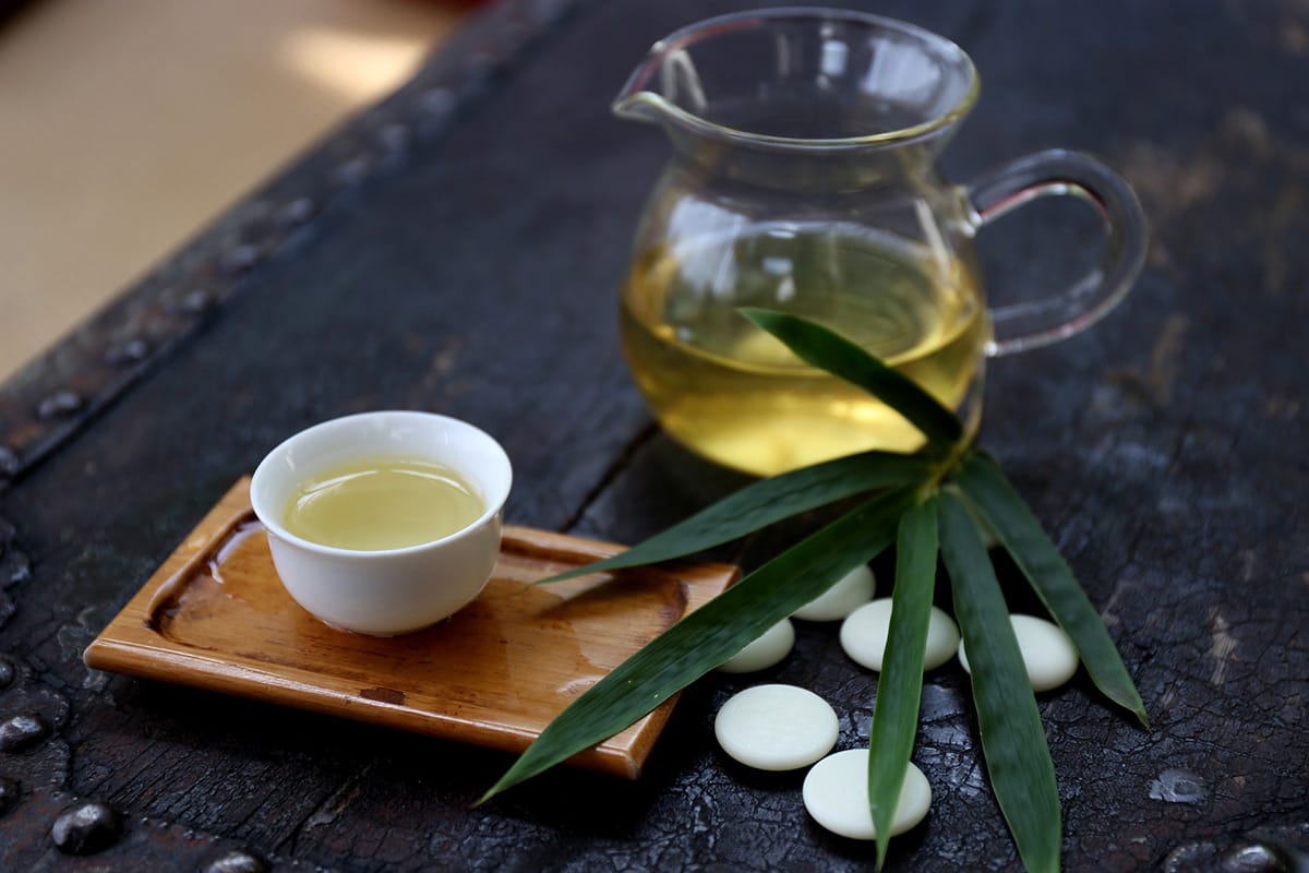Cup of bamboo tea and glass tea can with bamboo tea on a table with bamboo leaf, pebbles, and little tray as decoration