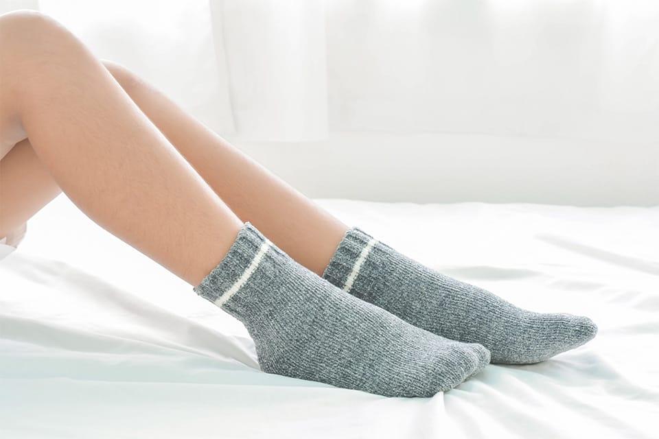 Person wearing grey bamboo socks on a bed