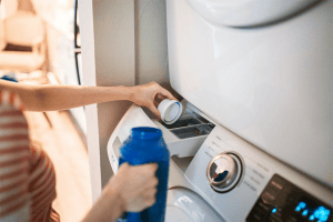Person holding blue plastic bottle to put detergent into machine