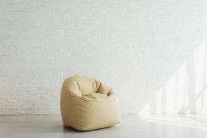 Sunlight near beige bean bag chair near brick wall in modern home