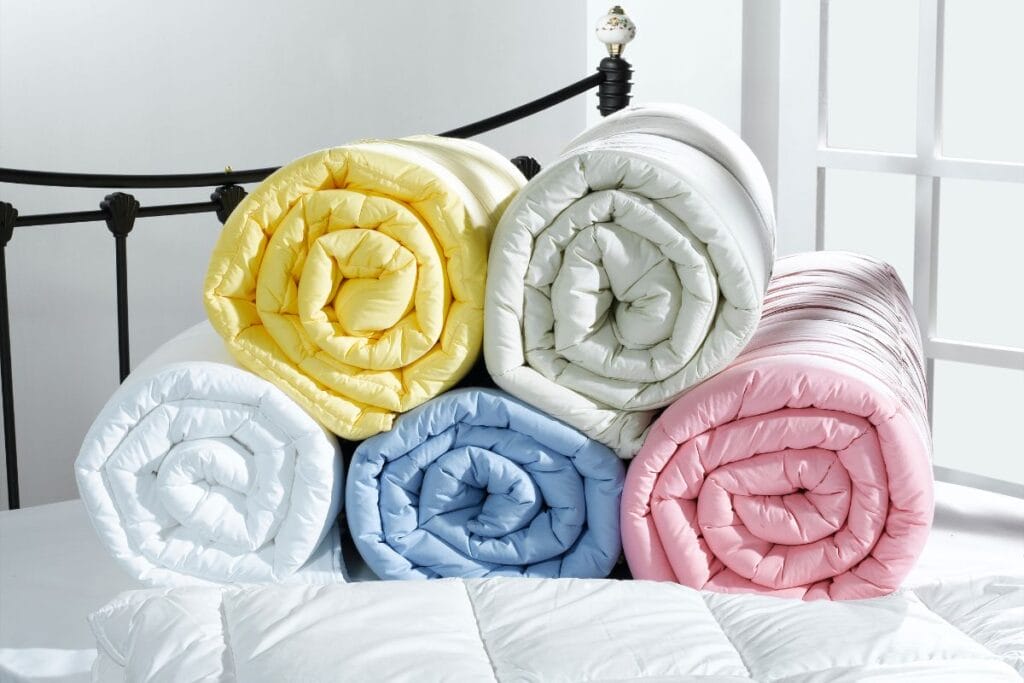 5 differently colored, rolled-up bamboo quilts on a bed