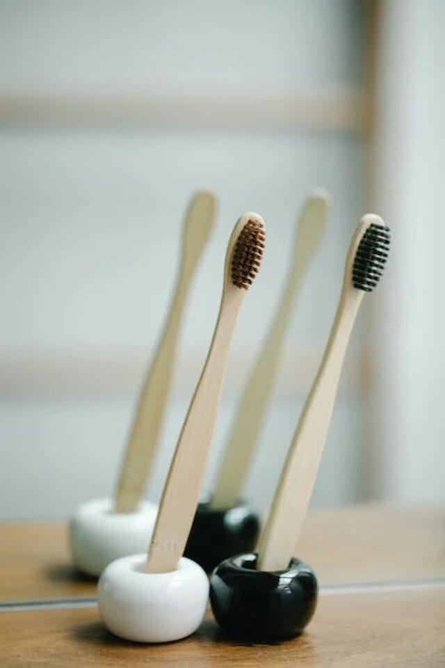 Two lightweight and minimal bamboo toothbrushes near a bathroom mirror.