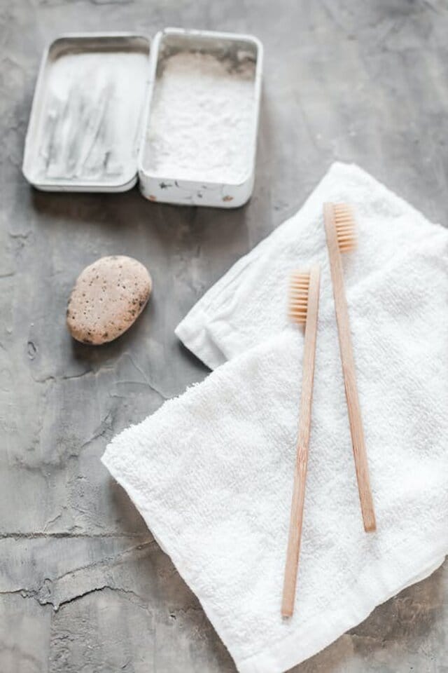 Bamboo toothbrushes placed in a white face towel with eco-friendly toothpaste on a bathroom sink as personal hygiene items.