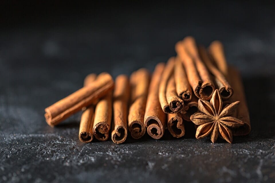 Several cinnamon sticks with star anise laying on a dark surface