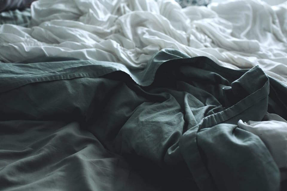 Messy white and dark green bamboo sheets on the bed
