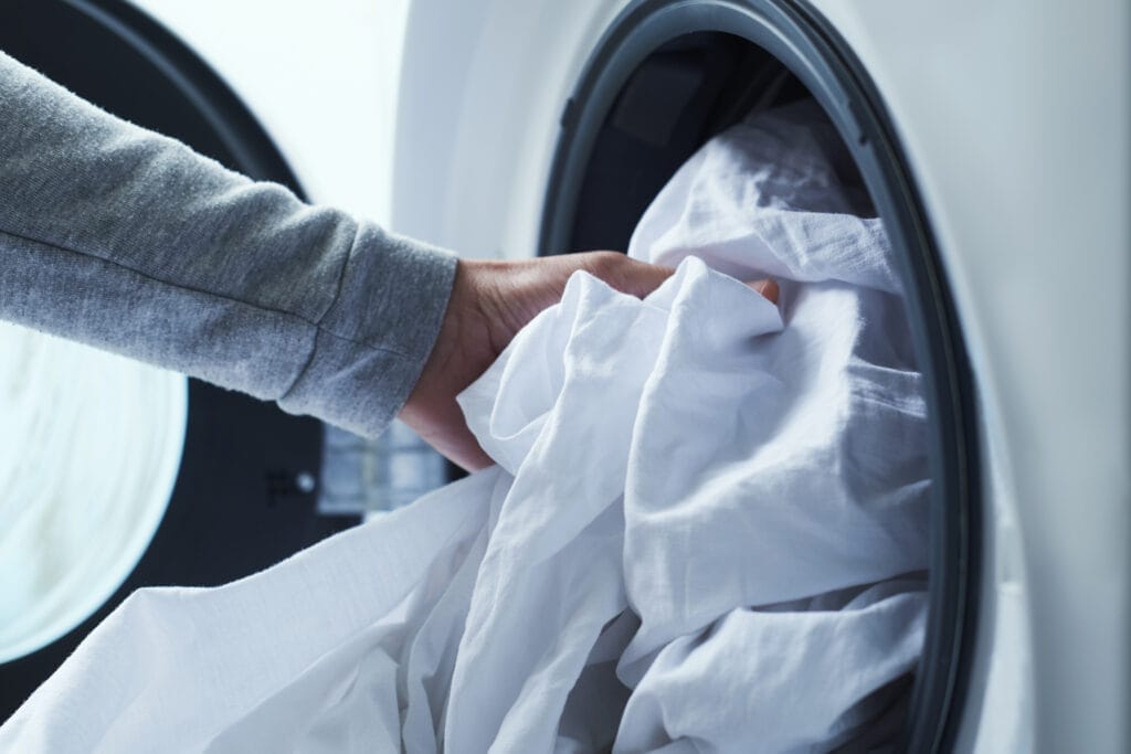 Closeup of a man putting white bamboo sheets into the washing machine